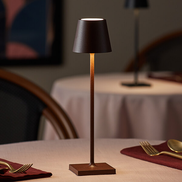 A small, rust-colored cordless rechargeable table lamp with a slim stem and conical shade, placed on a dining table.