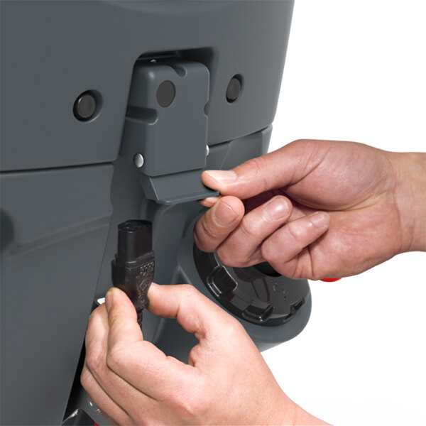 A close-up of hands connecting a power plug to a NaceCare Solutions TBL1620/50T 20" lithium-ion floor scrubber with traction drive and one NX1K battery.