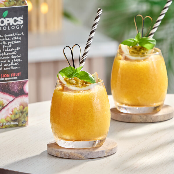 A glass of yellow-orange passion fruit frozen beverage garnished with a slice of fruit, mint, and a striped straw.