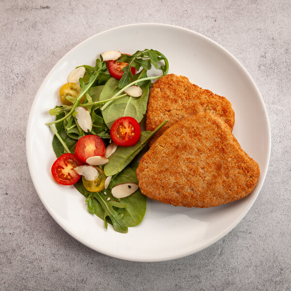 A plate with two breaded plant-based vegan chicken cutlets and a side salad with greens, cherry tomatoes, and sliced almonds.