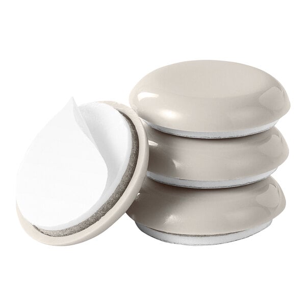A set of round, beige adhesive furniture sliders with a smooth top and a peel-off backing, shown in a stack.