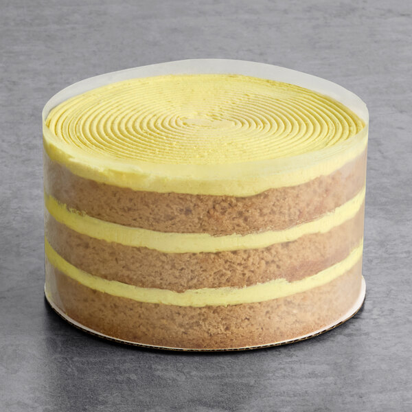 A round, four-layer vegan lemon naked cake with yellow frosting between the layers and on top, partially wrapped in a clear plastic collar.