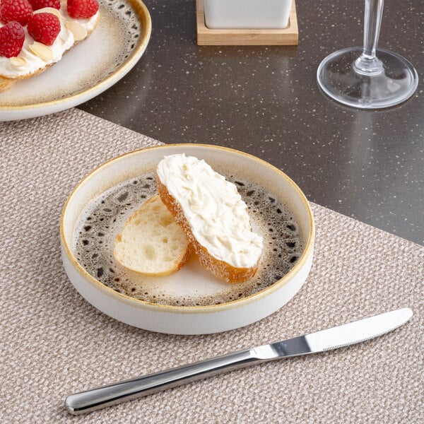 A round brown and cream porcelain plate with a raised rim and spotted edge, holding slices of bread with cream spread.