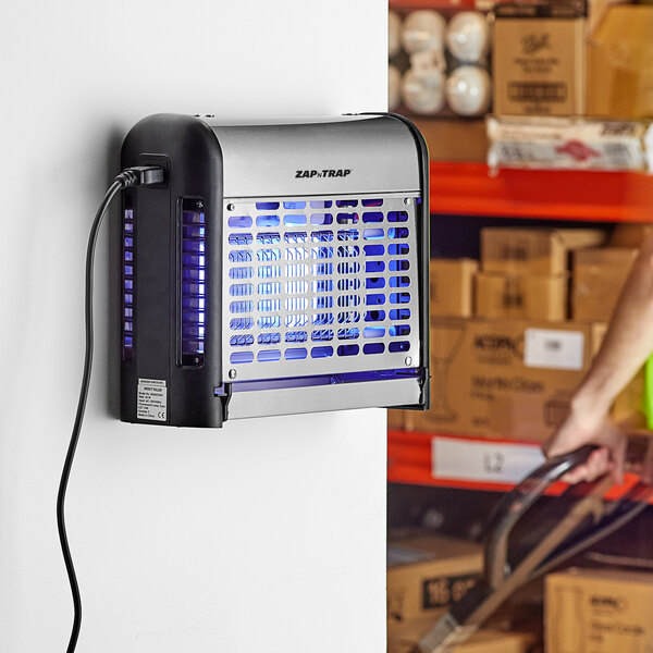 A stainless steel indoor LED insect trap and bug zapper mounted on a wall in a storage area.