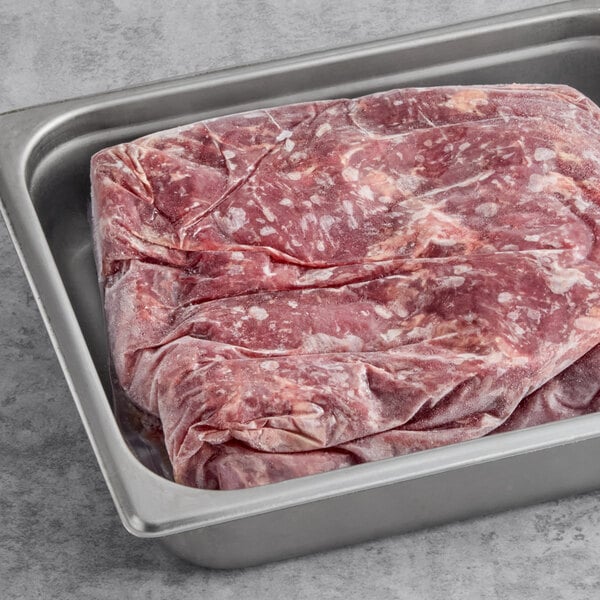 A large frozen slab of tenderized skirt steak in a metal tray.
