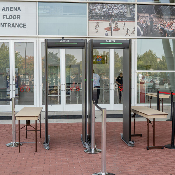 A pair of Garrett Paragon ADA-compliant walk-through metal detectors set up at an arena entrance with tables on either side.