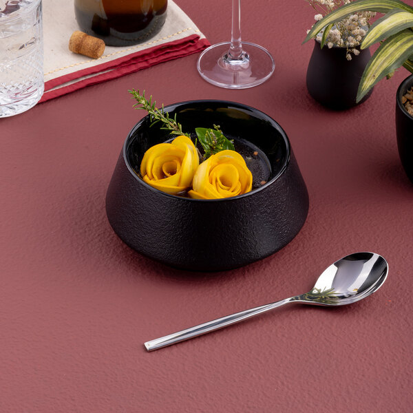 A black round porcelain coupe bowl with a modern design, containing a yellow garnish and herbs.