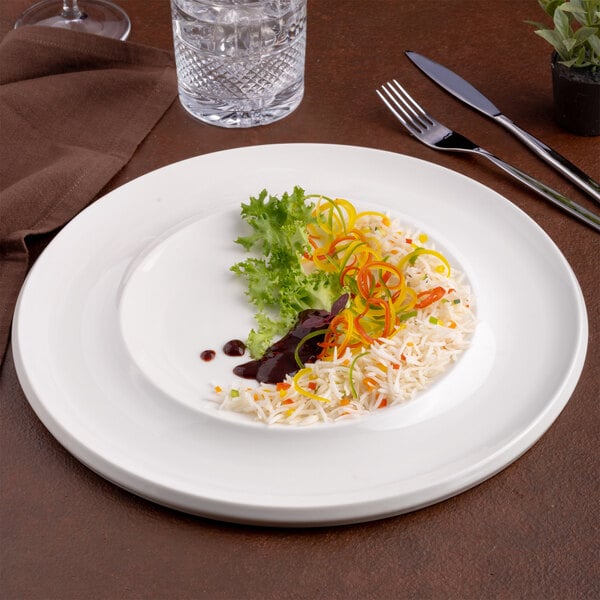 An ivory round wide rim porcelain plate with a small portion of rice, vegetables, greens, and sauce, displayed on a table setting.