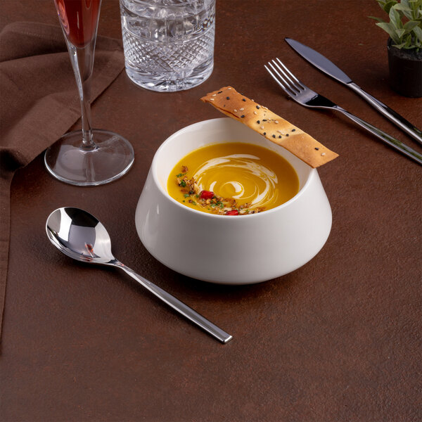 A round ivory porcelain coupe bowl filled with soup and garnished with a breadstick.