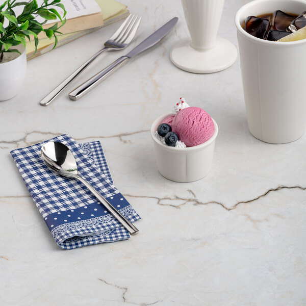 A small ivory round porcelain ramekin filled with a scoop of pink ice cream and blueberries, placed on a marble surface.