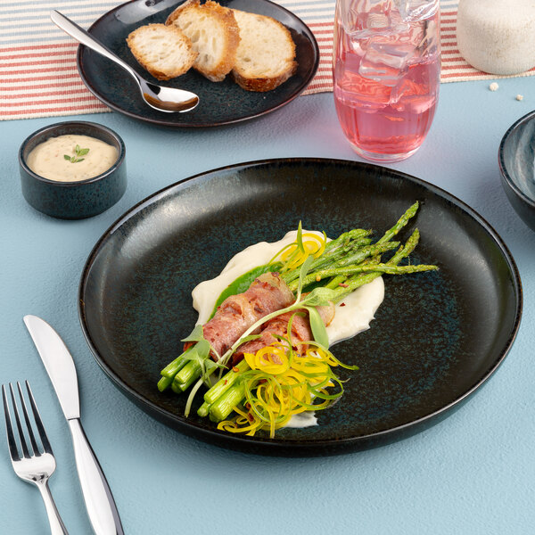 A black round porcelain coupe flat plate with a gourmet meal served on it.