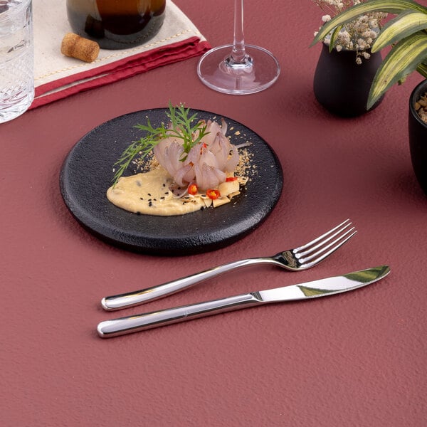 A small round black porcelain plate with a gourmet food presentation.