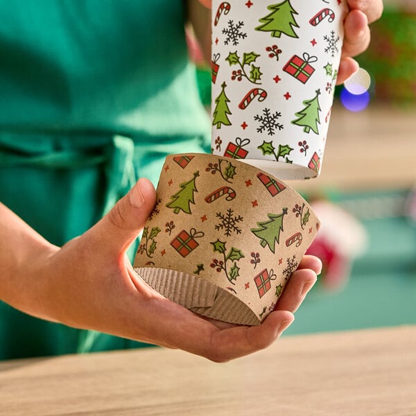 A festive coffee cup sleeve with a cartoon Christmas print featuring trees, presents, candy canes, and holly.