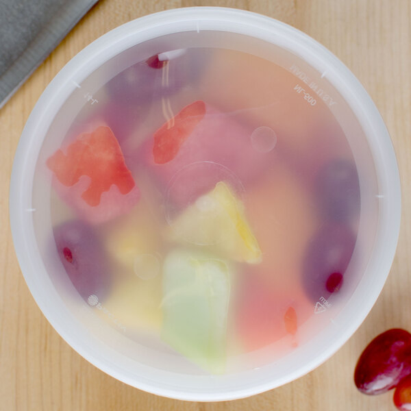 A white plastic Pactiv deli container filled with fruit on a counter.