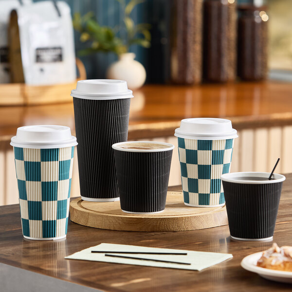 A set of black and checkered double wall ripple paper hot cups with white lids displayed on a wooden surface.