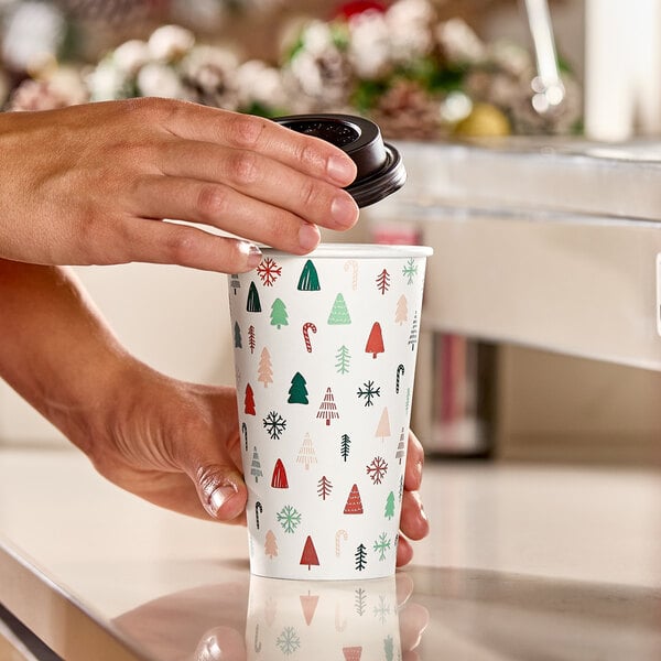 A 16 oz. paper hot cup with a modern Christmas print featuring trees, snowflakes, and candy canes.