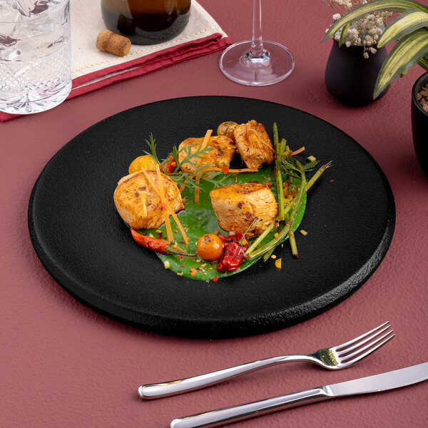 A black round porcelain plate with a gourmet food presentation.