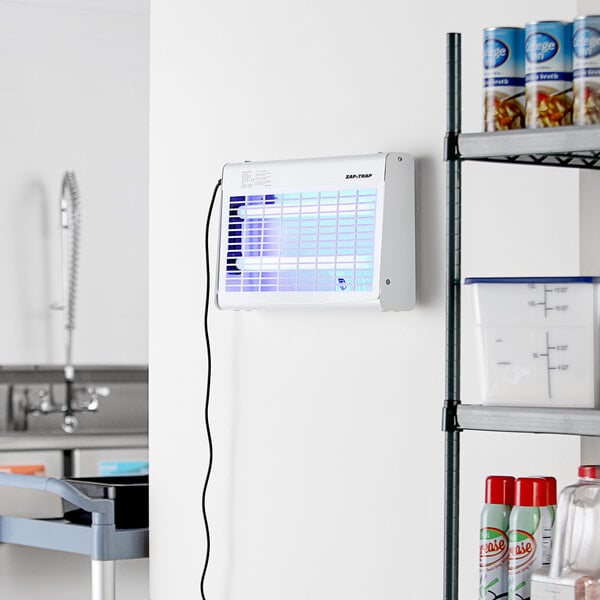 A white indoor LED insect light trap mounted on a wall in a kitchen or storage area.