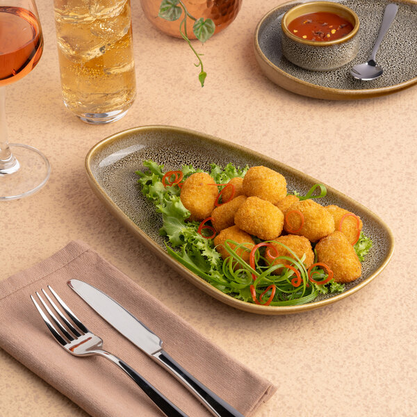 An oval asymmetric brown porcelain platter with a raised rim, displayed with food on a table setting.