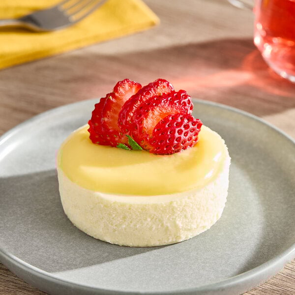 A small round yuzu cheesecake topped with sliced strawberries, served on a gray plate.