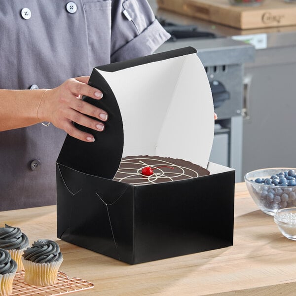 A black bakery box with an open lid containing a cake, displayed on a kitchen counter.