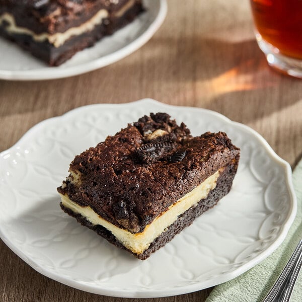 A chocolate brownie bar with a creamy filling and Oreo cookie pieces on top, served on a white plate.