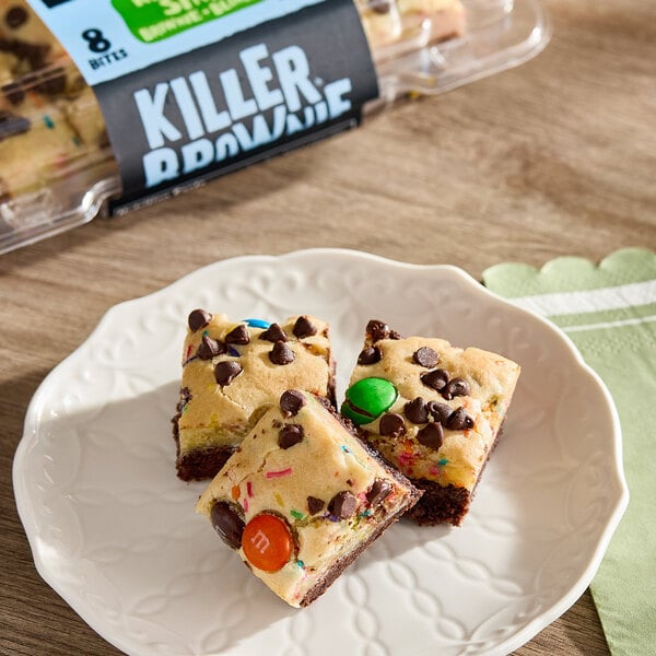A plate with three brownie bites topped with chocolate chips and colorful candy pieces, with a package labeled 'Killer Brownie' in the background.