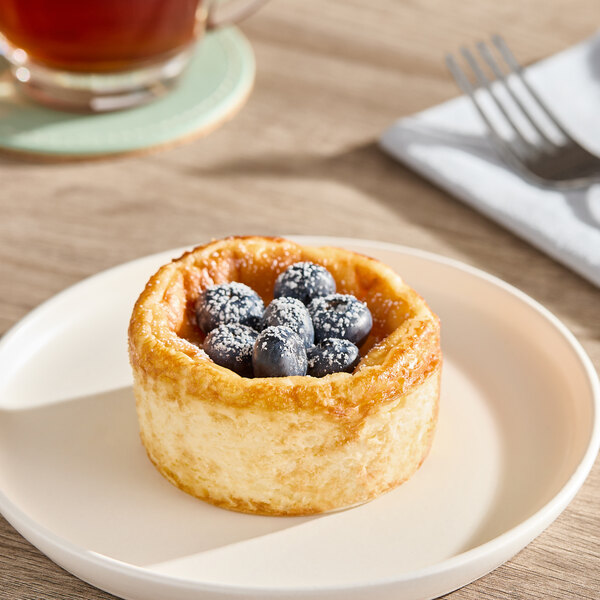 A small Basque cheesecake topped with fresh blueberries and a dusting of powdered sugar on a white plate.