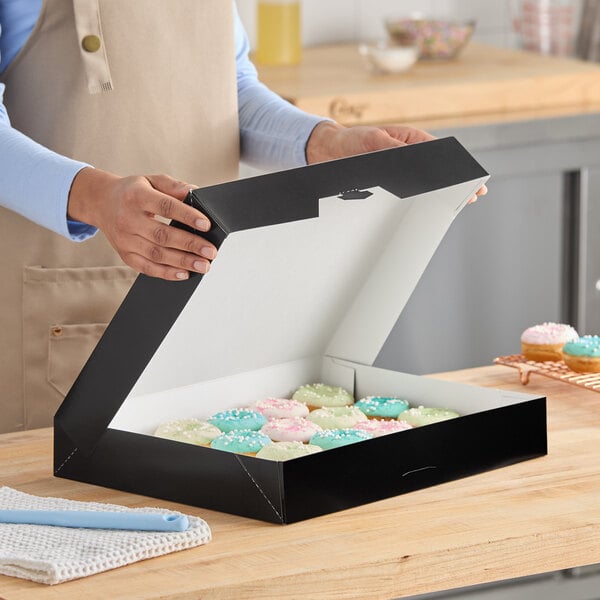 A black auto-popup bakery box filled with assorted donuts on a wooden countertop.