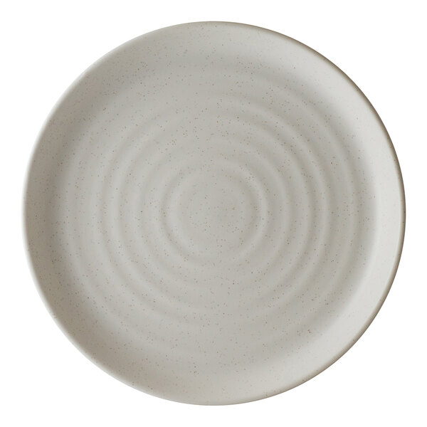 A round, light-colored porcelain plate with a subtle speckled pattern and concentric circular ridges.