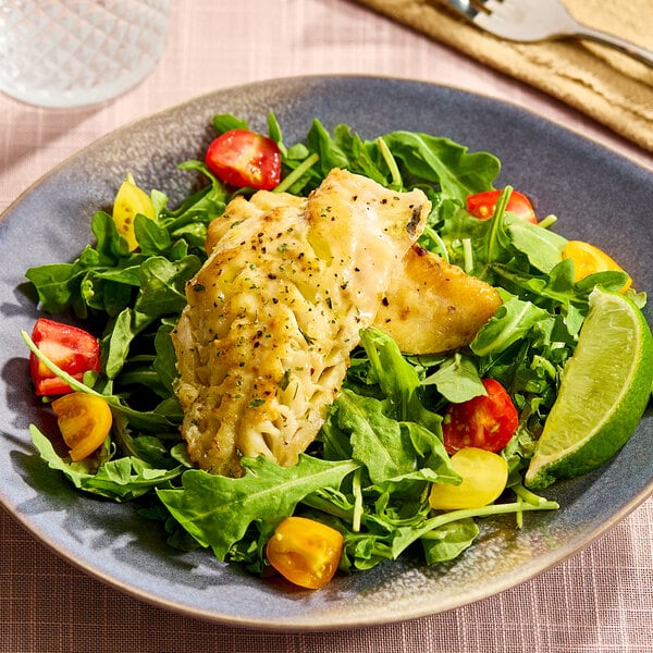 A plate of cooked ocean perch fillet served on a bed of fresh greens with cherry tomatoes and a lime wedge.