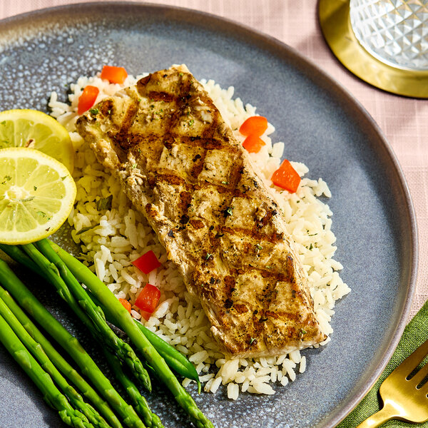 A grilled boneless skinless mahi mahi steak served on a bed of rice with asparagus and lemon slices.