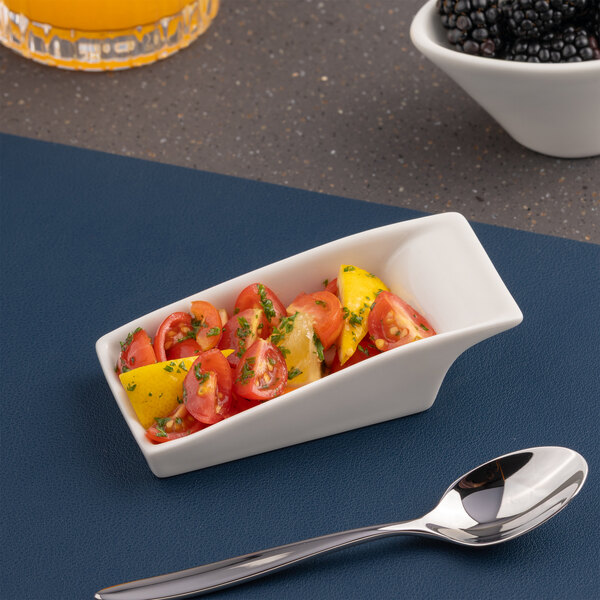 A small ivory rectangular slanted porcelain coupe bowl filled with a tomato and herb salad.
