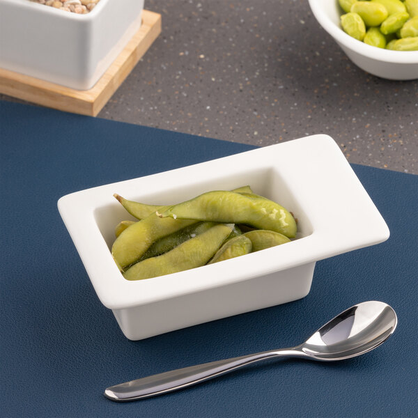 A small rectangular ivory porcelain bowl with an offset wide rim, filled with green edamame pods.