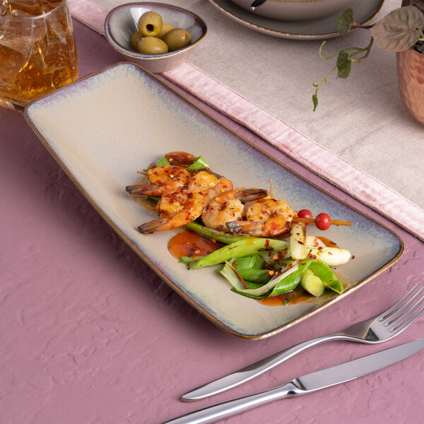 An asymmetric rectangular beige porcelain coupe platter with a food presentation, placed on a pink and beige table setting.
