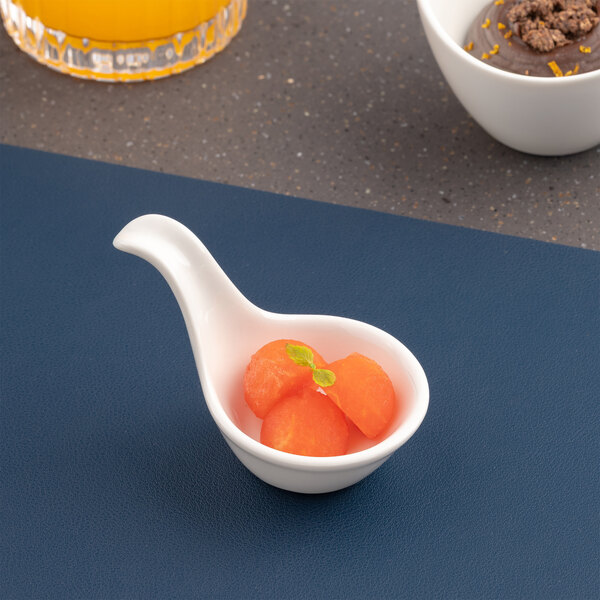 A small ivory porcelain coupe bowl with a handle, containing three melon balls and a mint garnish.