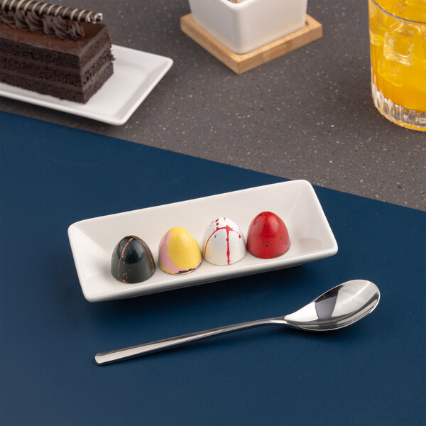A small ivory rectangular porcelain bowl with a wide rim, shown holding four colorful chocolates.