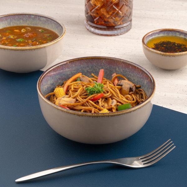 A beige round porcelain coupe bowl filled with noodles and vegetables.