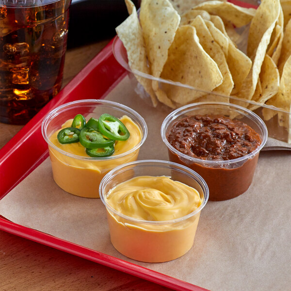 A table with a tray of chips and three containers of chili sauce.