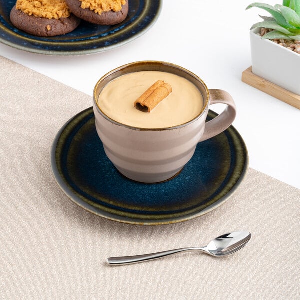 A blue porcelain tea cup with a matching saucer, filled with a creamy beverage and garnished with a cinnamon stick.