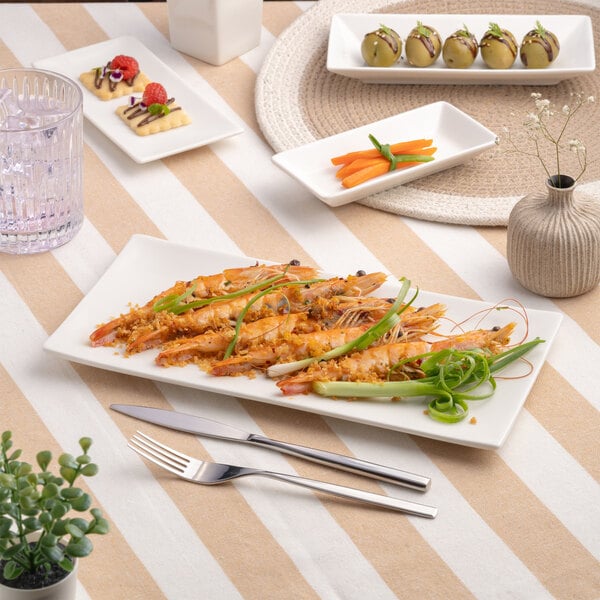 A rectangular ivory porcelain coupe platter displaying a seafood dish, placed on a striped tablecloth with other small plates and tableware.