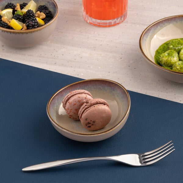 A small beige round slanted porcelain coupe bowl containing two chocolate macarons.