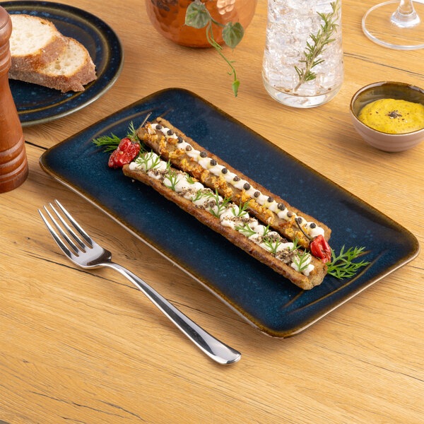 A blue rectangular porcelain platter displayed on a wooden table with food and utensils.