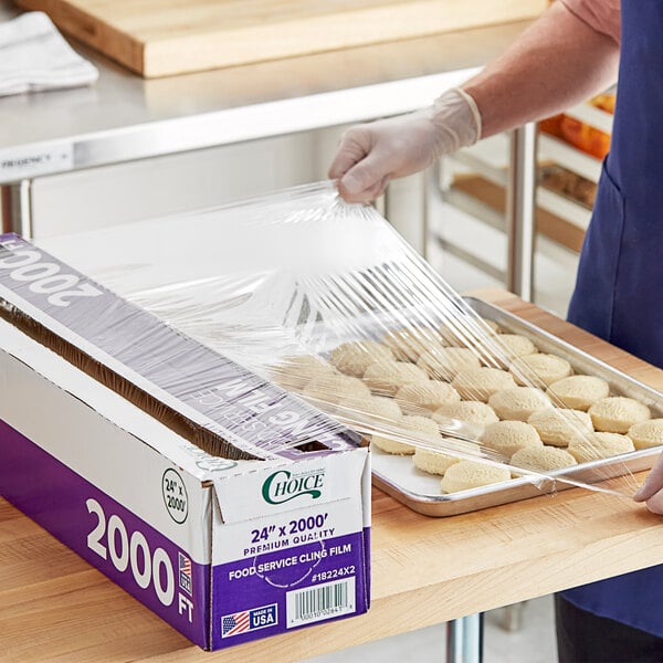 A large box of Choice 24-inch by 2000-foot foodservice cling film with a serrated cutter being used to cover a tray of food.