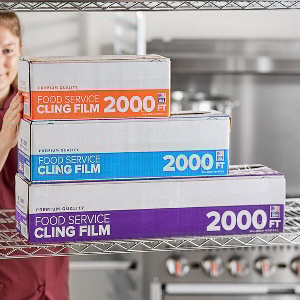 A stack of three boxes of Choice 24" x 2000' foodservice cling film with serrated cutters on a metal shelf.