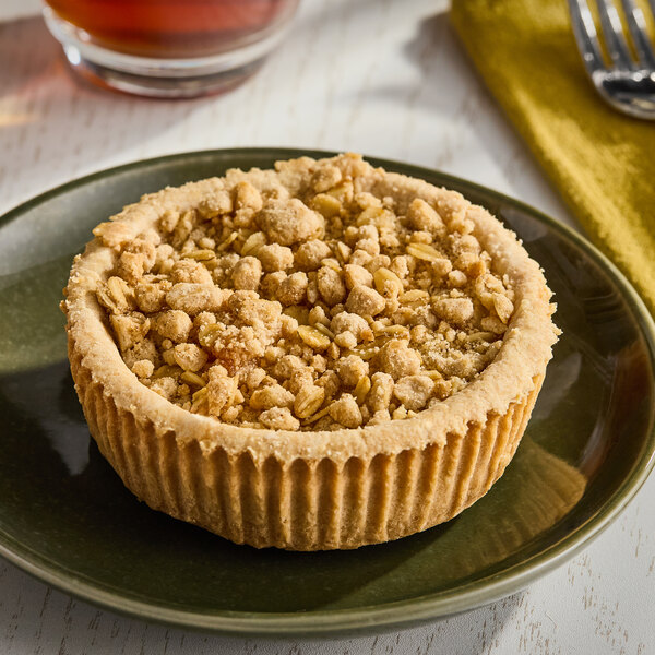 A mini apple crumb pie with a crumbly oat topping on a green plate.