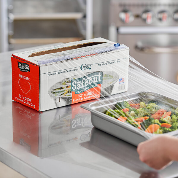A box of Choice Safecut 12-inch by 2000-foot premium foodservice film with a slide cutter being used to cover a tray of vegetables.