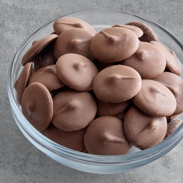 A glass bowl filled with round Guittard milk chocolate compound coating wafers.