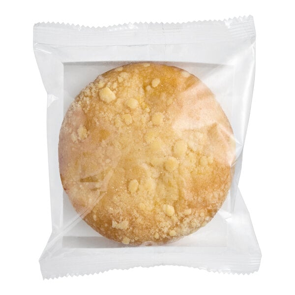 A round vegan pineapple crumb cake individually wrapped in clear plastic packaging.