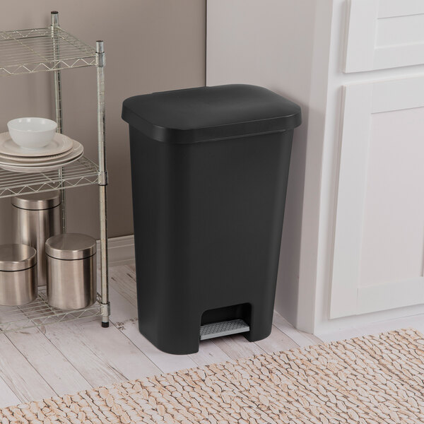A black rectangular step-on wastebasket placed in a kitchen setting.